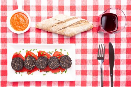 Slices of Spanish black pudding on piquillo peppers in white plate on a red checkered tablecloth. Spanish tapas.の写真素材