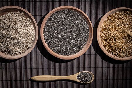 Sesame, chia and flax seeds in wooden dishes, wooden spoon with chia on wooden base. Top view.の写真素材