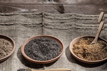 Sesame, chia and flax seeds in wooden dishes, wooden spoon with chia on wooden base.の写真素材