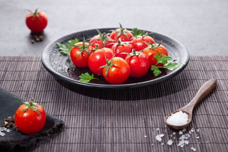Fresh cherry tomatoes on black round plate, on dark background.の写真素材