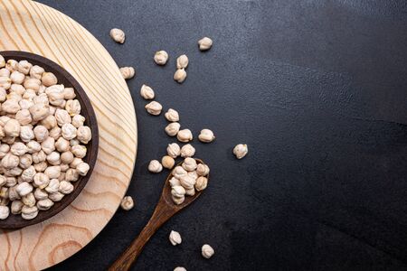 Chickpeas on wooden plate and wooden spoon on black background with copy space. Top view.の写真素材