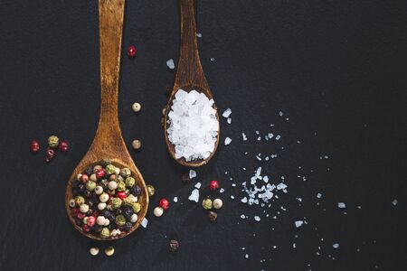wooden spoons with pepper and salt on a blackboard base, top view with copy space. Cooking ingredients and condiments concept.の写真素材