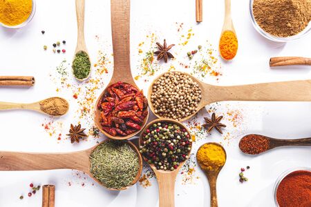 Variety of spices and herbs in spoons and bowls on white background. Top view. Cooking ingredients and condiments concept.の写真素材