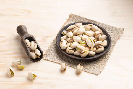 Pistachios on wooden spoon and dish on light wooden base.