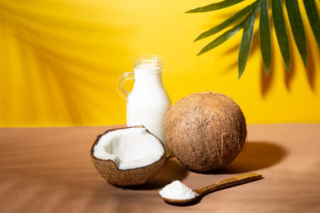 Coconuts, coconut milk and shredded coconut on yellow and brown background with palm shades.