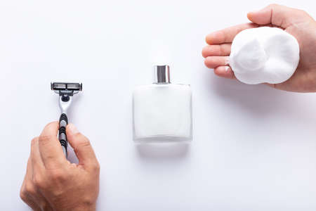 Hands holding razor blade and shaving foam, with after shave isolated on white background top view....