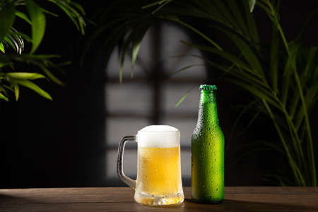 Beer mug and bottle on dark background on wooden base.の写真素材