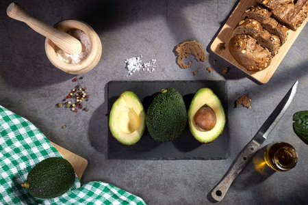 Flat lay composition with avocados on dark table with window shades.