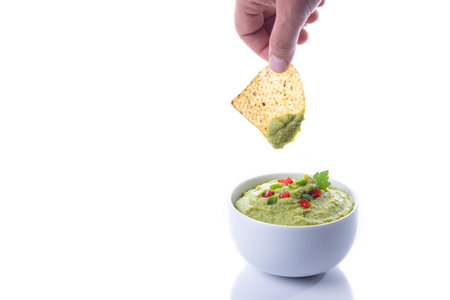 Hand dipping nachos in guacamole isolated on white background with copy space.の写真素材