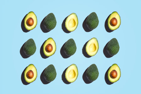 Symmetrical composition of avocados slices on blue background. Top view.