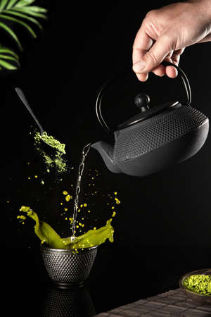 Water poured into a dark cup of matcha tea on a black background. Vertical format.