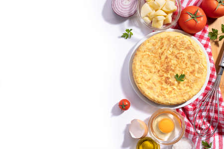 Traditional Spanish omelette with potatoes and onion with ingredients on white background with copy...