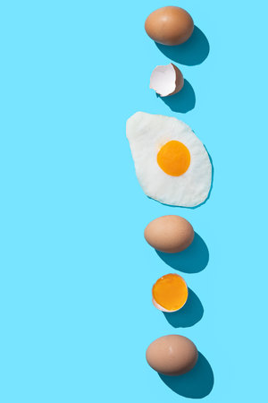 Fresh brown eggs, egg yolk and fried egg on blue background with copyspace. Vertical format.の写真素材