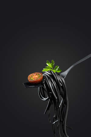 Black pasta rolled on a fork isolated on black background with copyspace. Vertical format. Cooking concept.の写真素材