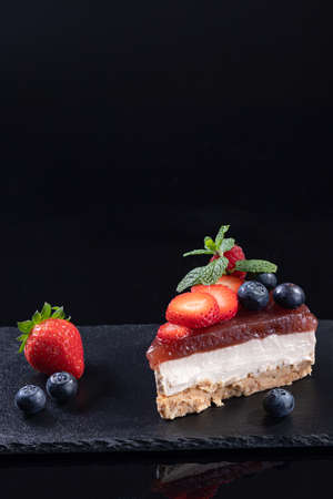 Piece of cheesecake isolated served on slate plate on black background with copyspace. Portrait...