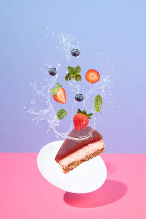 Flying cheesecake and strawberries with blueberries with splash on pink and blue background with...