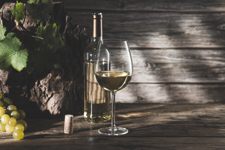 Elegant glass of wine and white wine bottle with grapes and shadows on dark wood background with copyspace.の写真素材