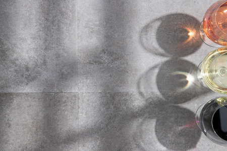 Red, white and rose wine in wine glasses with deep shadows on concrete background with copy space....