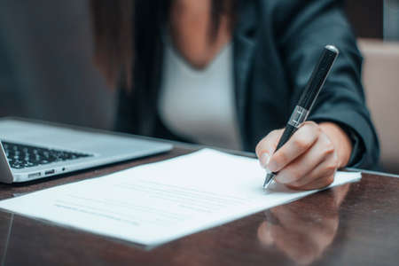 Young formal woman signing an employment contract on a paper next to her computer in the officeの写真素材
