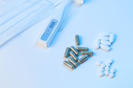 electronic thermometer, protective mask and tablets pills lie on a white background with blue...