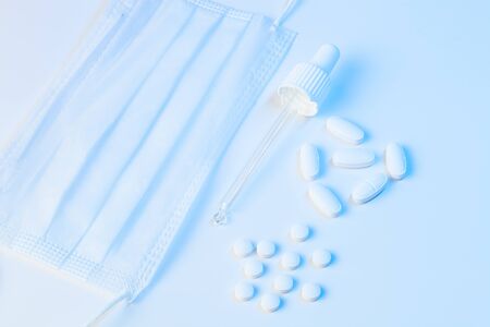 electronic thermometer, protective mask, pipette and tablets pills lie on a white background with blue illuminationの写真素材
