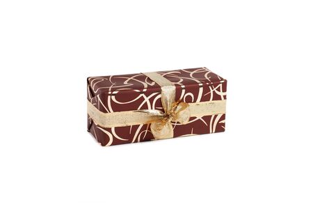 packaged rectangular gift in dark brown packaging with gold bow and gold pattern on a white backgroundの写真素材