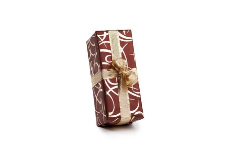 packaged rectangular gift in dark brown packaging with gold bow and gold pattern on a white backgroundの写真素材
