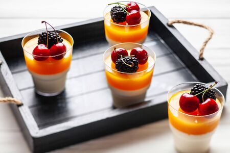 4 cups mango pannacota on wooden tray with blackberries and cherriesの写真素材