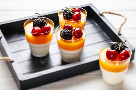 4 cups mango pannacota on wooden tray with blackberries and cherriesの写真素材