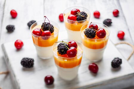 4 cups mango pannacota on wooden tray with blackberries and cherriesの写真素材