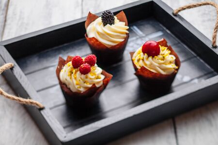 muffins with Belgian chocolate and white chocolate cream and mascarpone with berries on a wooden trayの写真素材