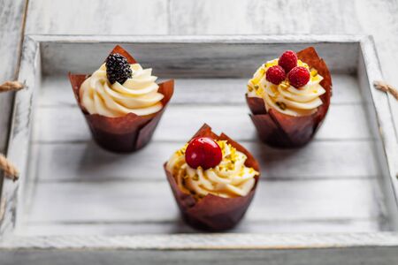 muffins with Belgian chocolate and white chocolate cream and mascarpone with berries on a wooden trayの写真素材