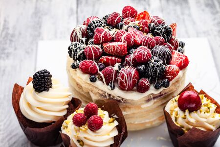 pancake cake with a cap of berries drenched in white chocolate on a wooden white table with a few Belgian muffinsの写真素材