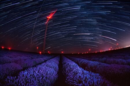 Beautiful landscape of a starry night with star trails over a field of lavender and red lights of wind turbines, Gorun, Bulgariaの写真素材