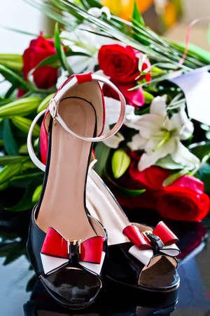 Beautiful shoes with red and white bow near a flower arrangement of red roses and white liliesの写真素材