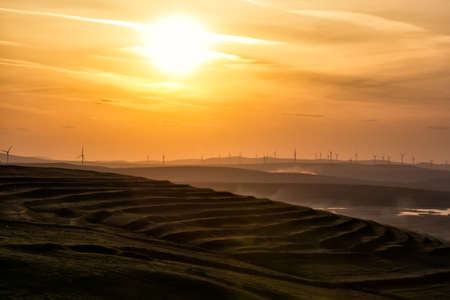 Beautiful rural landscape of a hill with a big setting sun and wind turbines, Dobrogea, Romaniaの写真素材