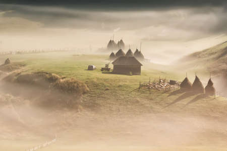 Beautiful rural mountain landscape in the morning light with fog, old houses and haystacks, Fundatura Ponorului, Hunedoara County, Romaniaの写真素材