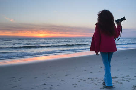 Beautiful young girl holding a camera and watching the sunset on the shore, Petten, Hollandの写真素材