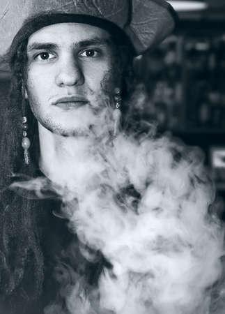 Beautiful young european man wearing a pirate hat and smoking, white heavy smokeの写真素材