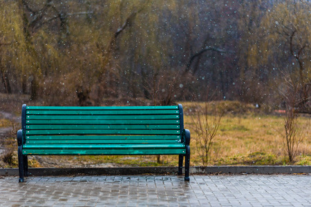 A green bench under falling snowflakes.の写真素材