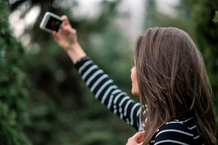 Young girl in striped sweater is taking picture of herself in the park. Shallow depth of field.の写真素材