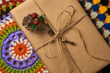 Wrapped book tied with brown paper thread with small dried bouquet of field plants is lying on the table on two colorful knitted napkins.の写真素材
