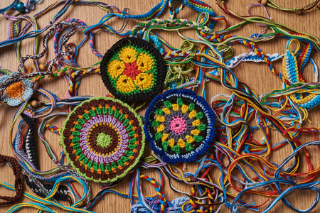 Different kind of knitted colorful bracelets and earrings are chaotically lying on the table. In the lower left side there are three big knitted amulets.の写真素材