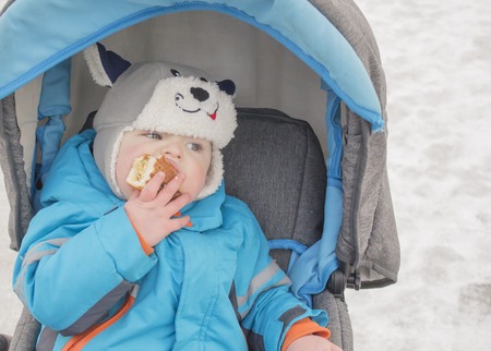 little boy sitting in the stroller in the winter and eats cakeの写真素材