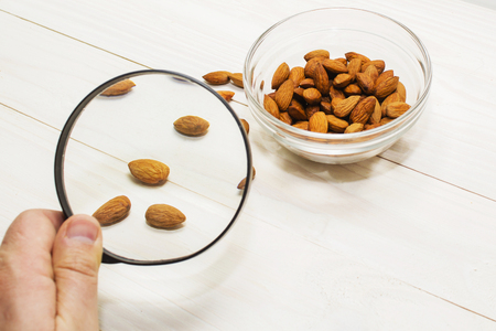 a lot of almonds in glass containers, on a light wooden background, magnifying glassの写真素材