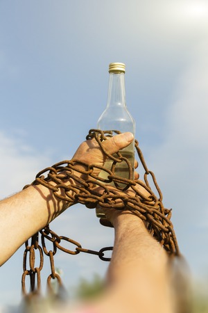Hand chained to a bottle of alcohol, against the blue sky.の写真素材