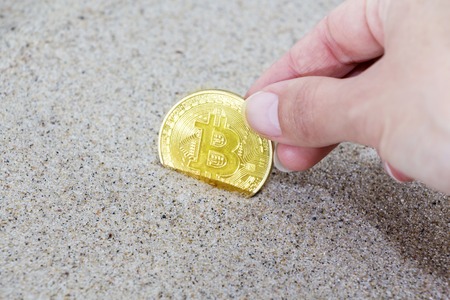 Coin bitcoin buried in the sand. Bitcoin is the most popular cryptocurrency in the worldの写真素材