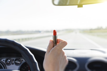 Woman putting a red lipstick while sitting in a car.の写真素材