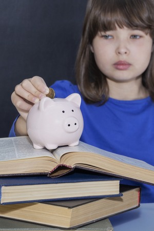 Teen puts coins in the piggy bank. The concept of paid education.の写真素材