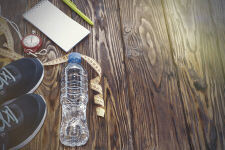 Healthy lifestyle and sports background. Sports shoes, Notepad and pen, and water bottle on wooden background with copyspace, topview.の写真素材